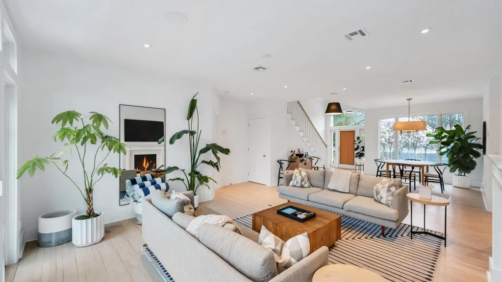 A bright living room with light-colored seating, plants, and a wooden coffee table.