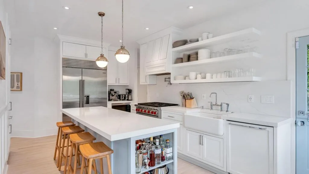 A bright kitchen with a long island, open shelves, and stainless steel appliances.