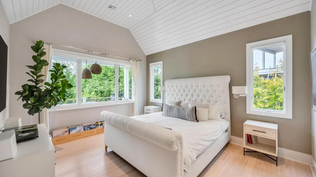 A bright bedroom with a large bed beneath a sloped, paneled ceiling.