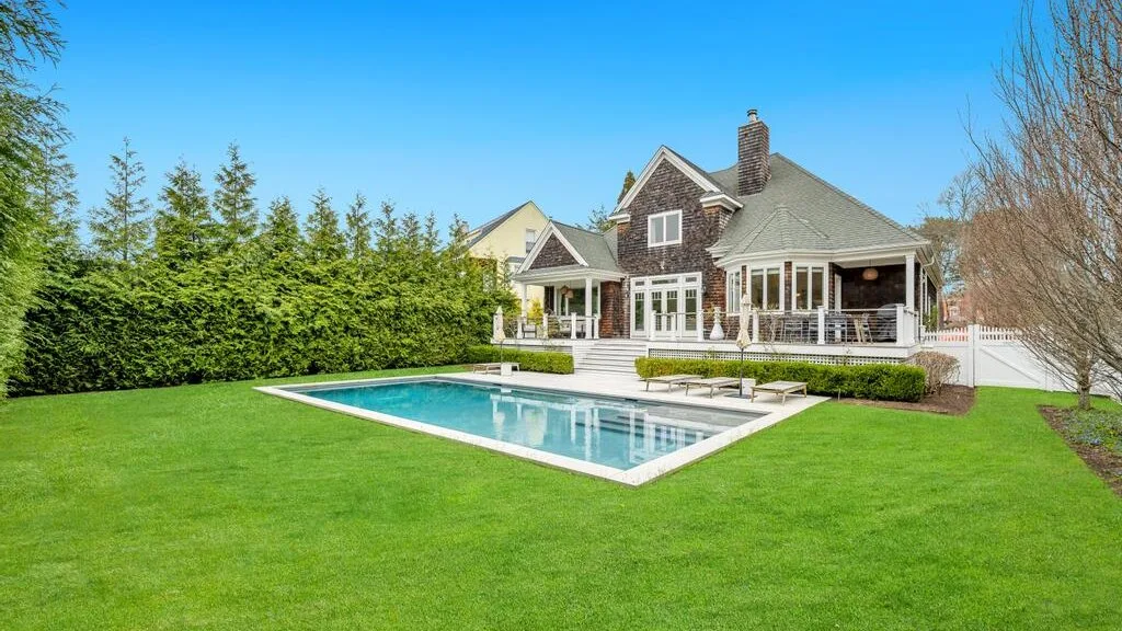 A landscaped backyard with a swimming pool and a large house.