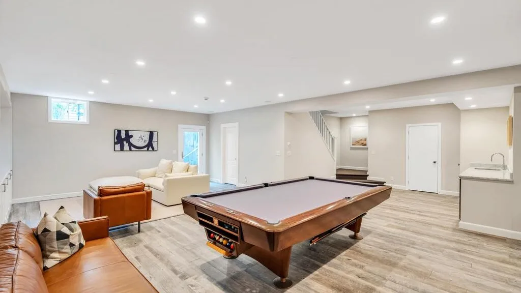 A finished basement game room centers on a pool table with seating along the side.