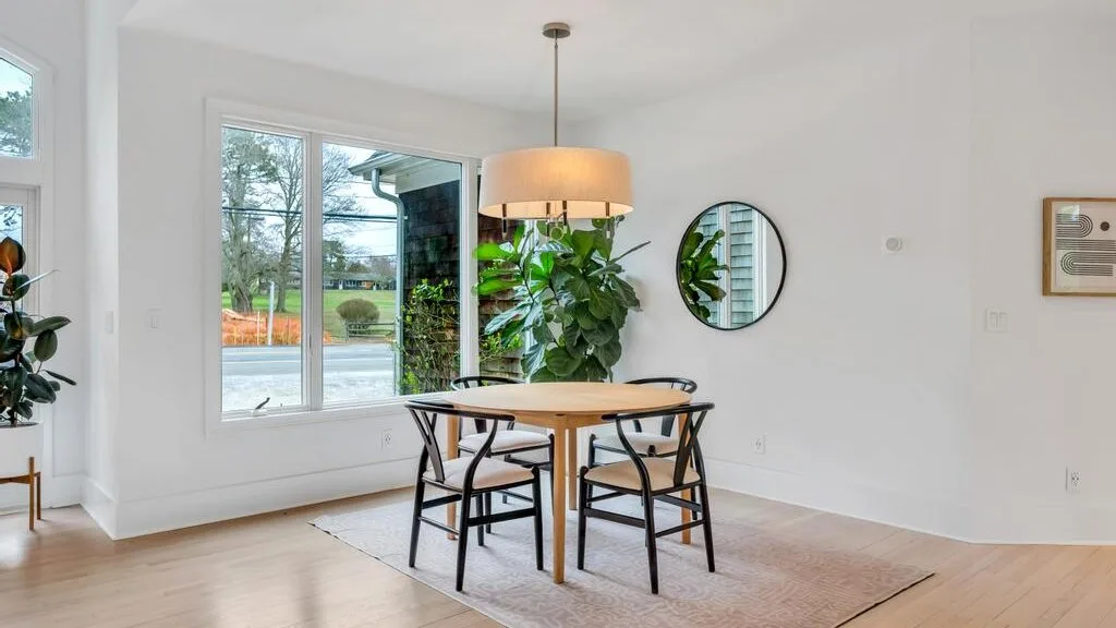 A bright dining area with a round table, chairs, and a large window.