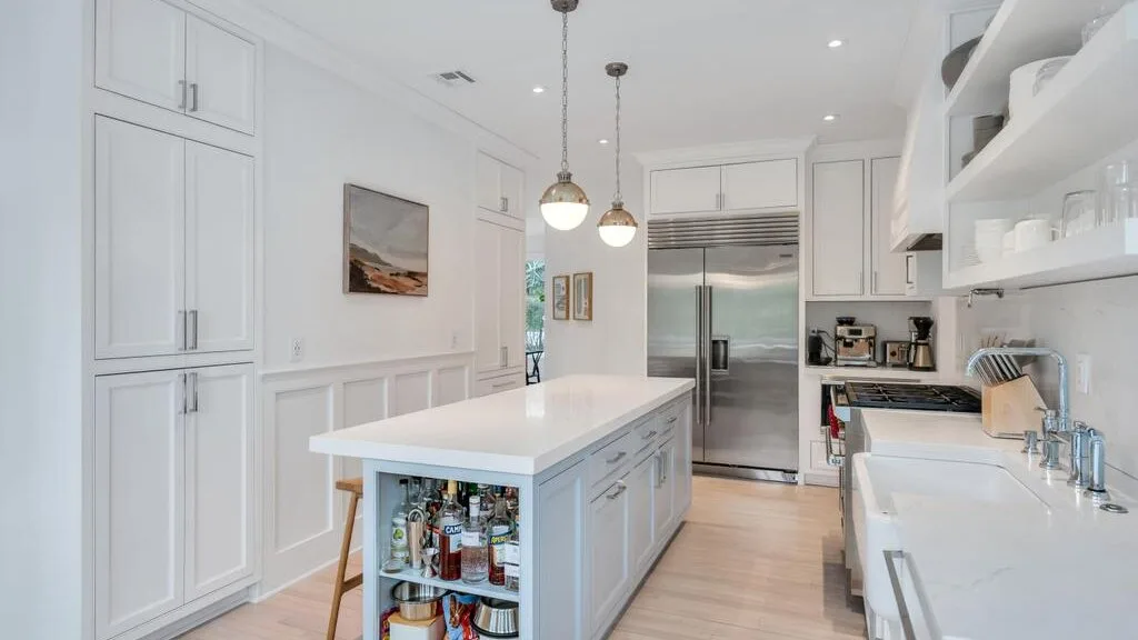 A bright kitchen with a central island and stainless steel refrigerator.