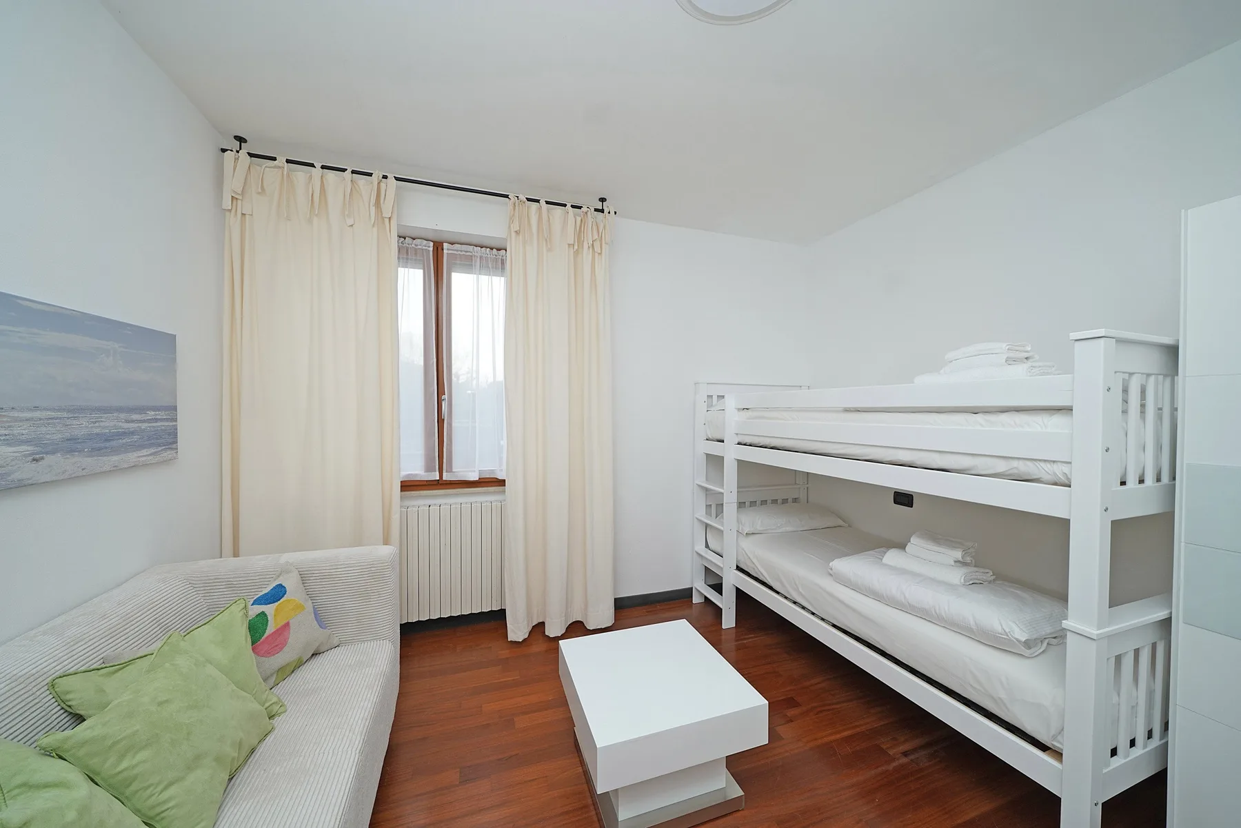 Un dormitorio luminoso con literas, un sofá y una pequeña mesa de centro.