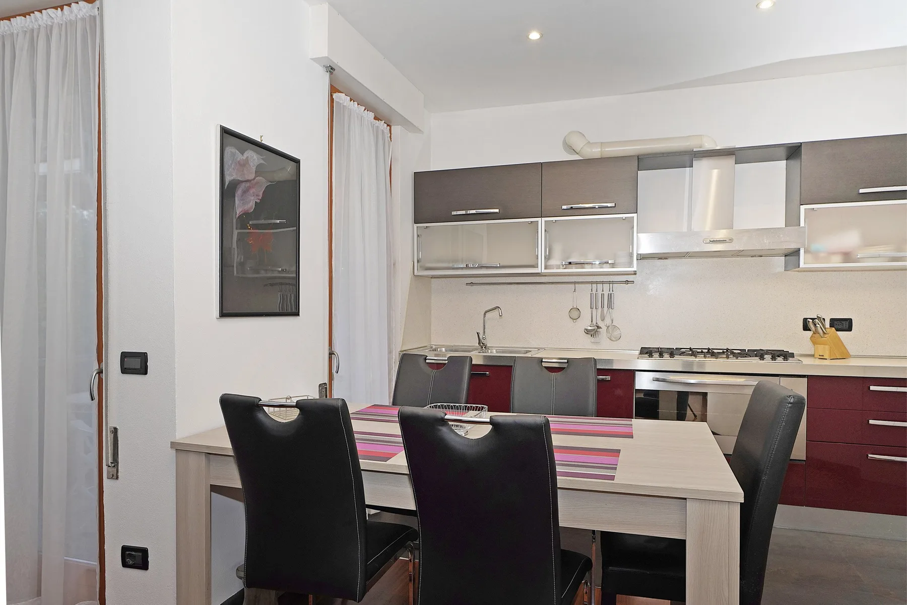Comedor con una mesa y asientos oscuros junto a una cocina moderna.