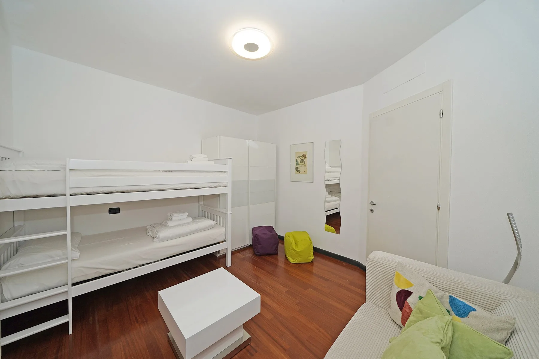 Un dormitorio luminoso con literas, una mesita y cojines de colores.