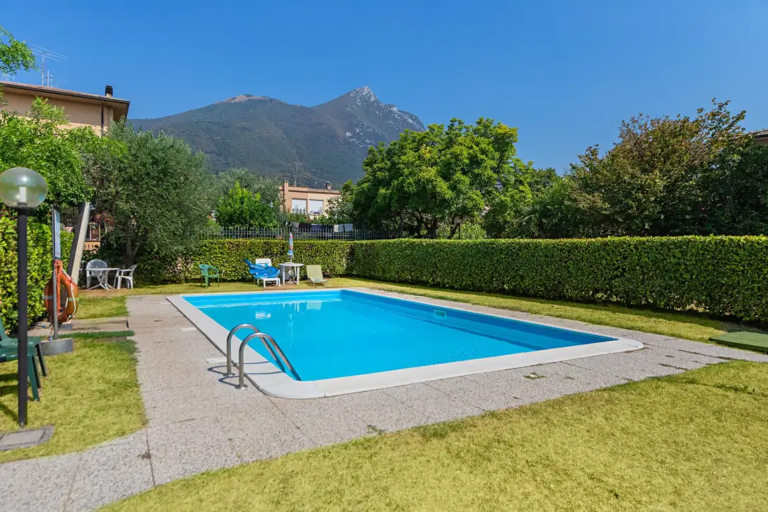 Piscina al aire libre rodeada de césped y setos, con montañas al fondo.