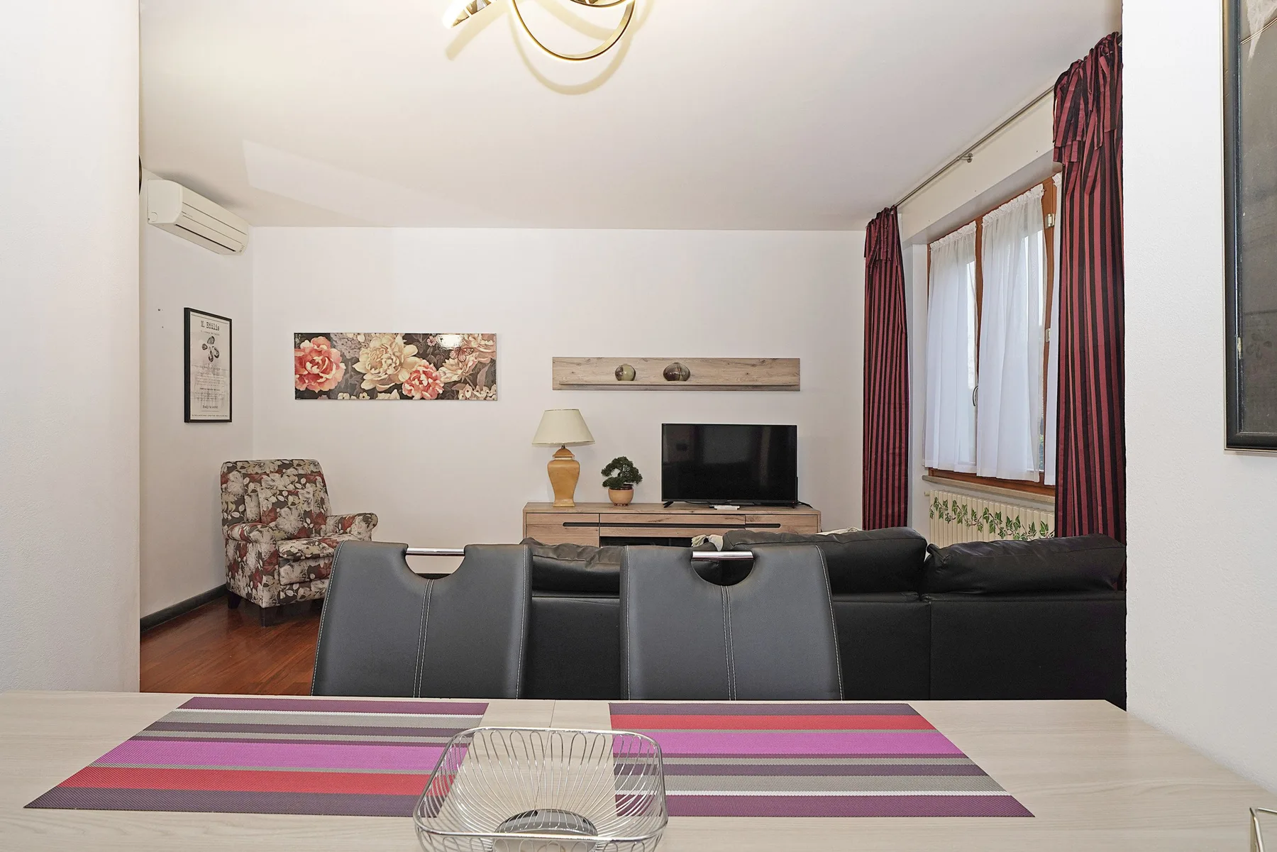 Una sala de estar con asientos, un televisor y una ventana grande con cortinas.