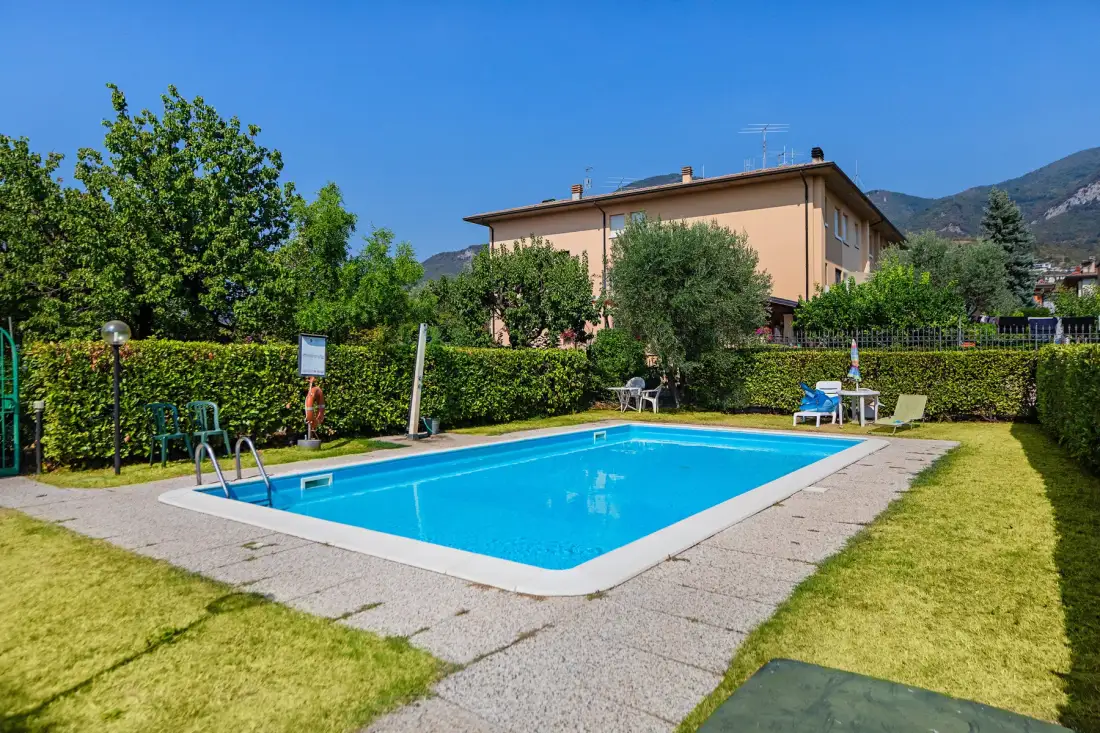 Una piscina está en un jardín junto a una casa, con montañas a lo lejos.