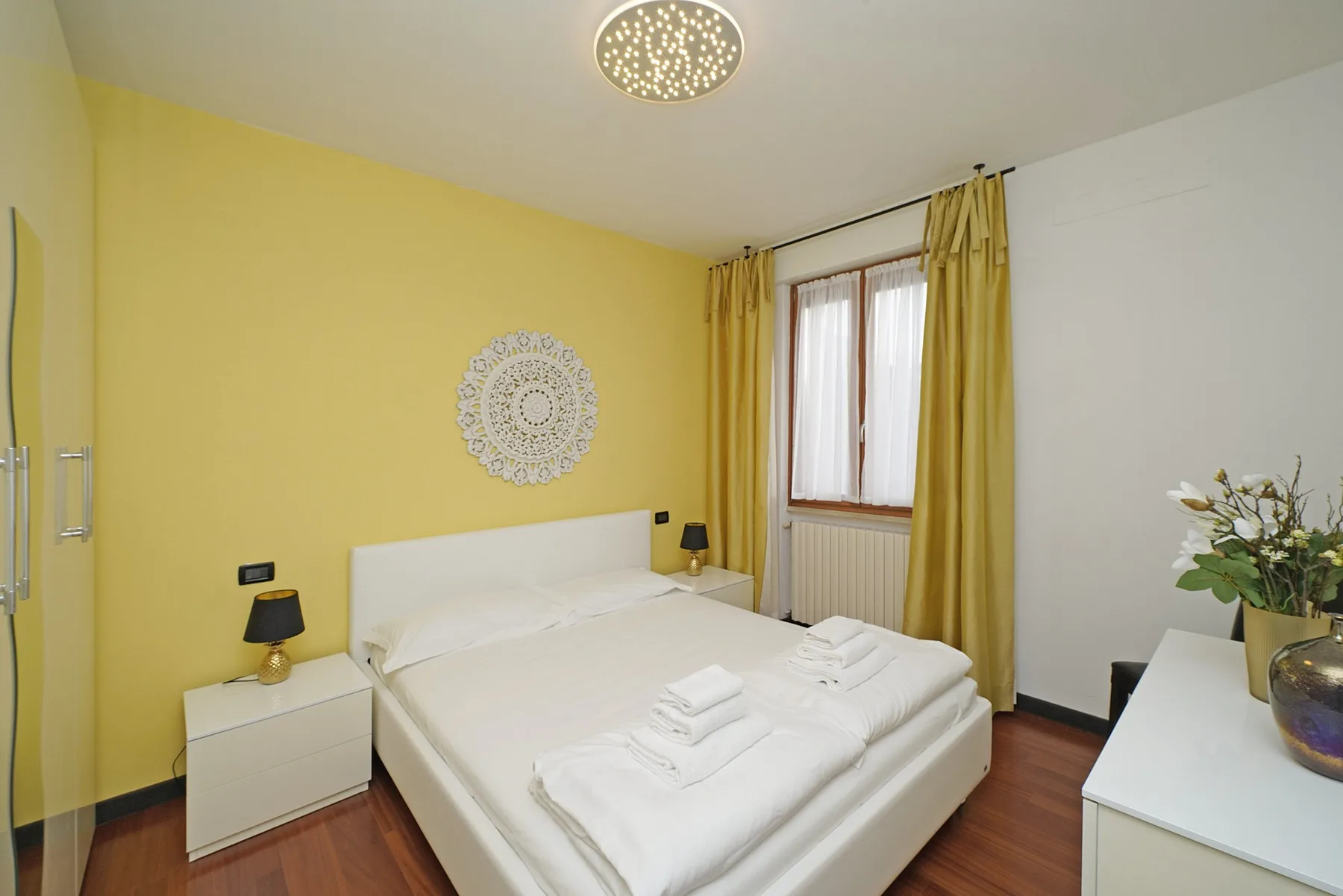 Un dormitorio con una cama ordenada, una mesita de noche y una ventana con cortinas.