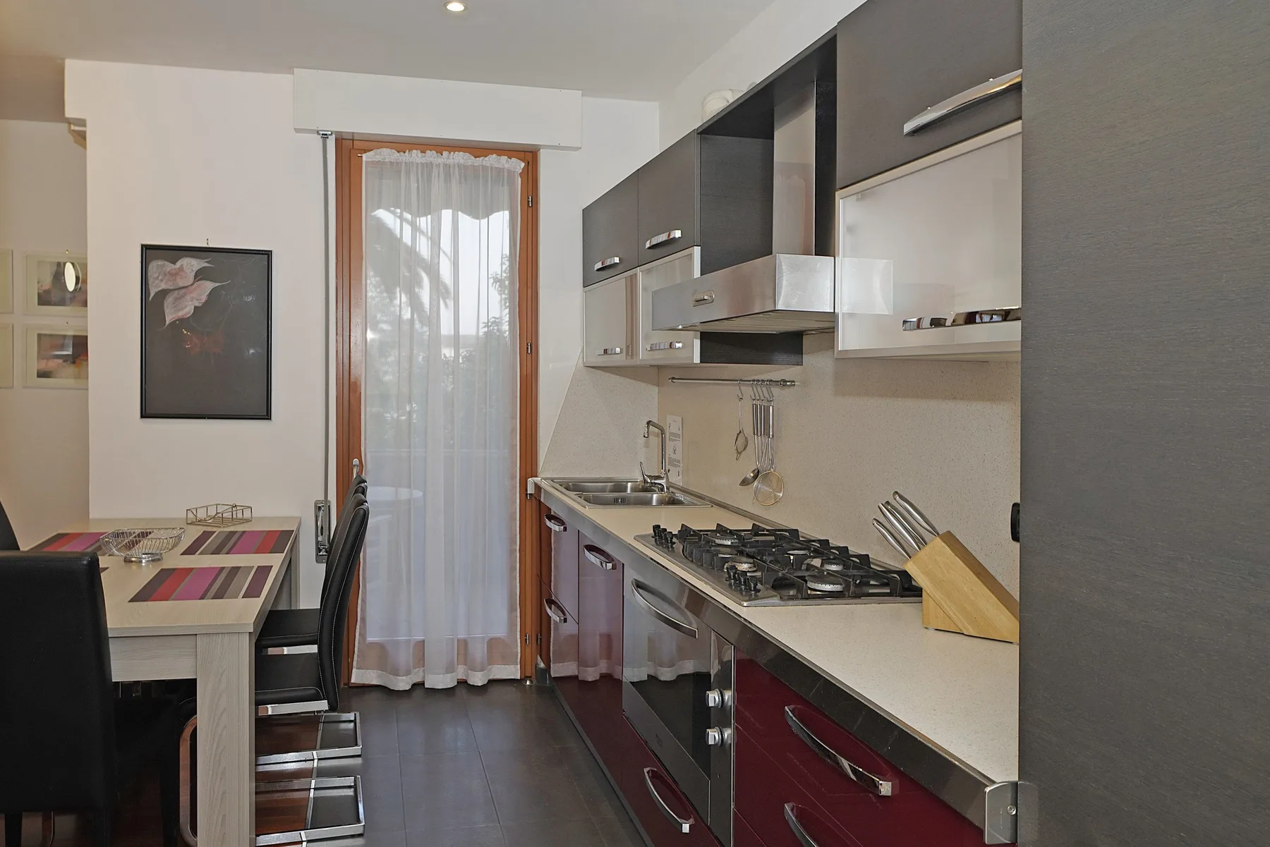 Una cocina estrecha con una mesa de comedor y una ventana con cortinas.