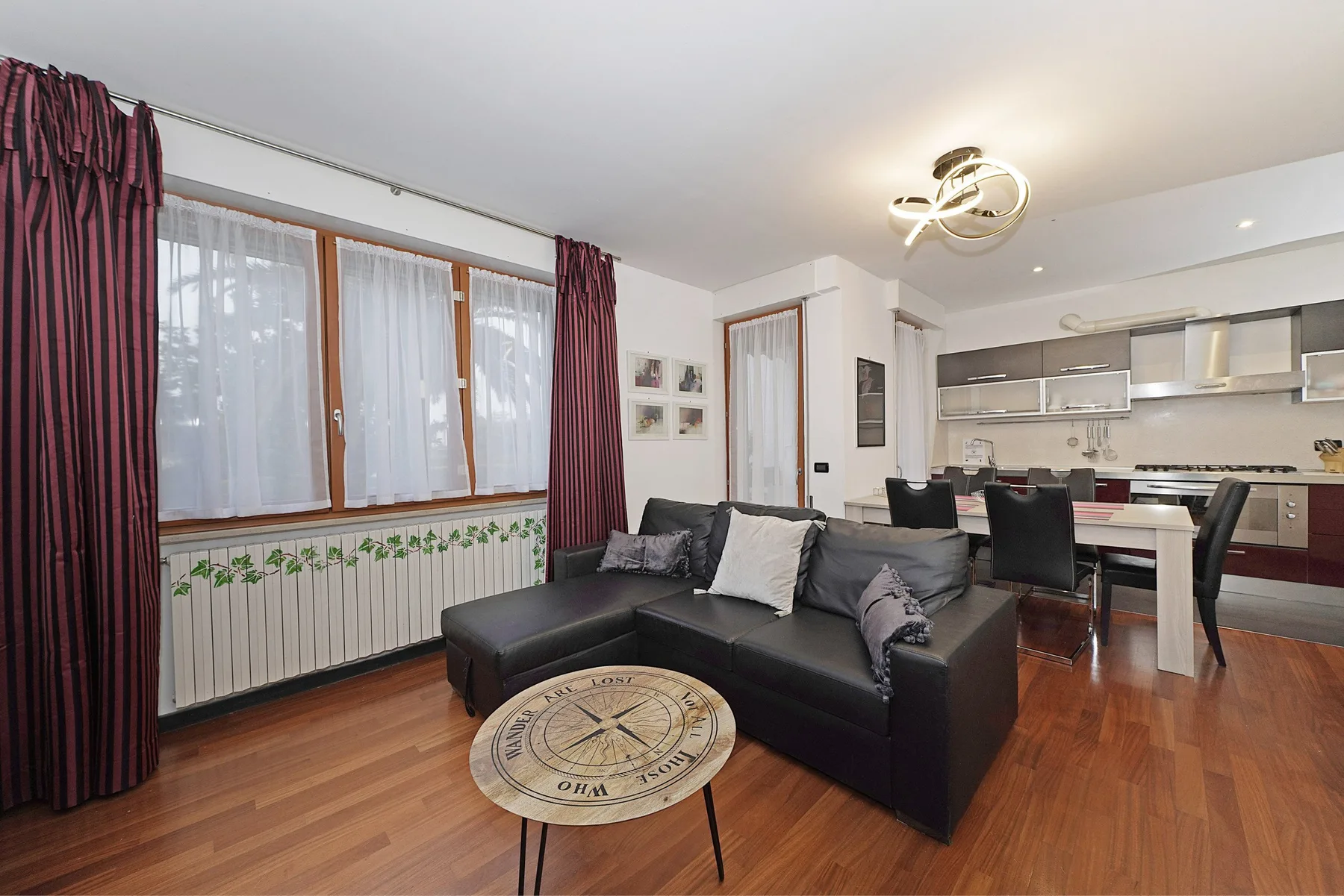 Una sala de estar con asientos oscuros junto a un comedor y una cocina.
