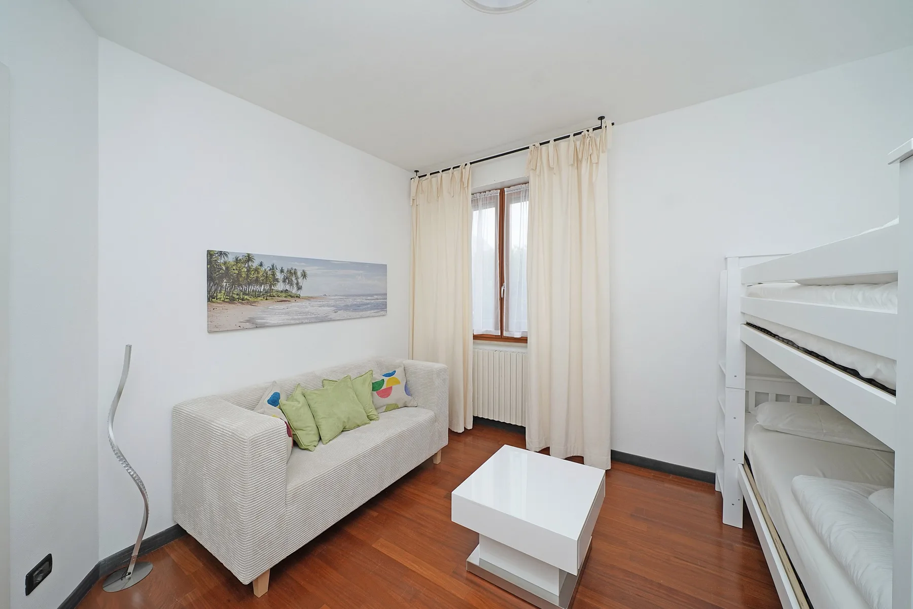 Una habitación luminosa con sofá, mesa de centro y literas blancas.