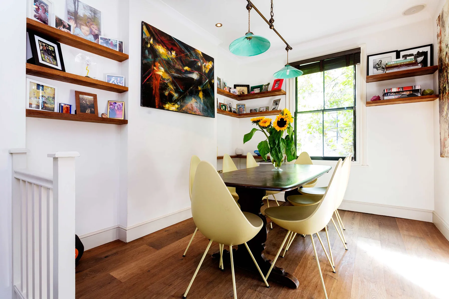 Comedor con mesa, asientos y flores junto a una ventana grande.