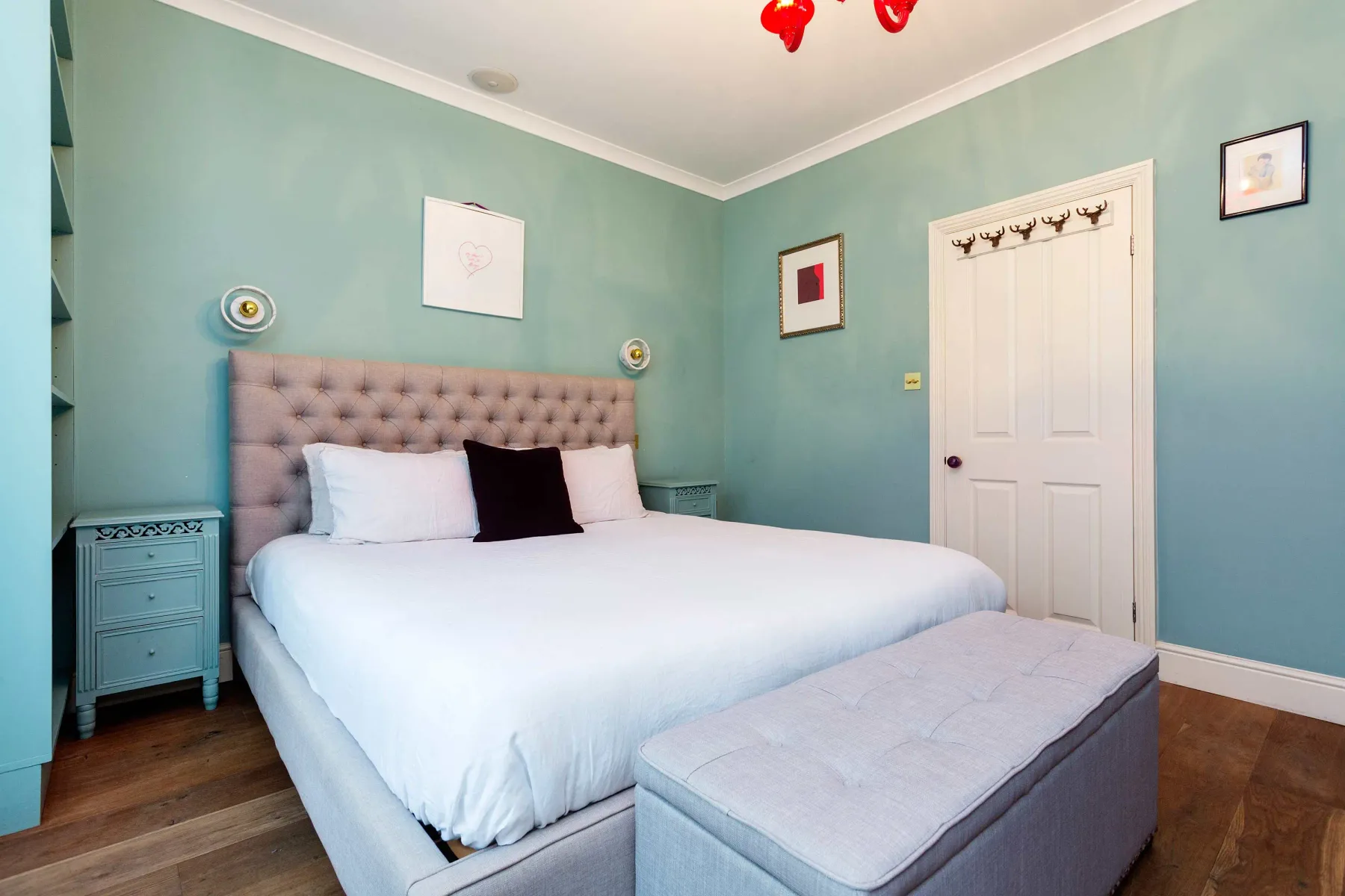 Un dormitorio con una cama grande, paredes azul claro y un banco acolchado a los pies.