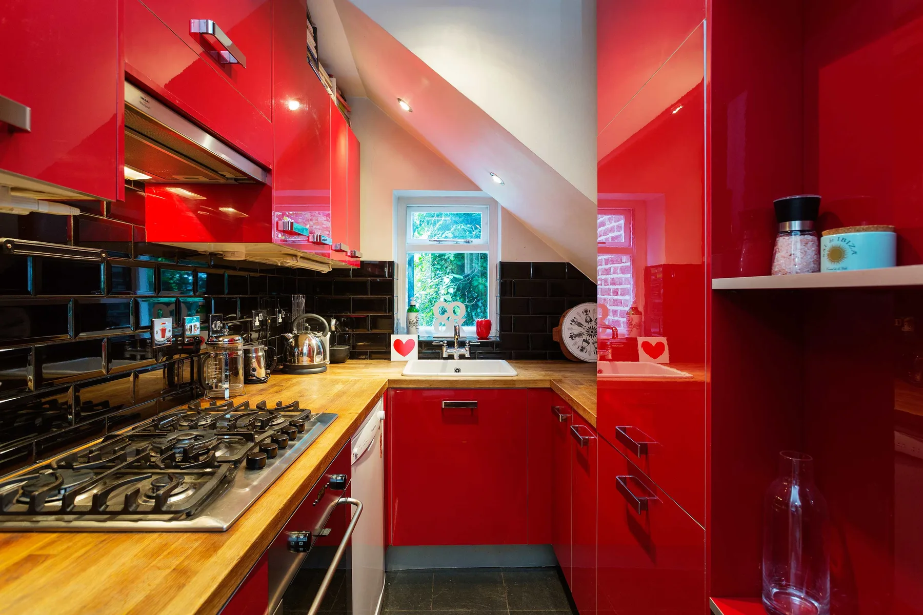 Una cocina compacta con gabinetes rojos, azulejos oscuros y una encimera de madera.