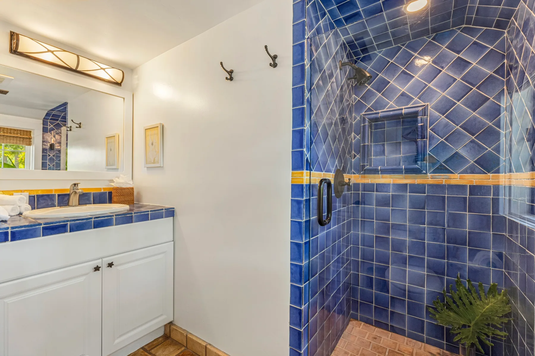 A bathroom with a white vanity and a blue-tiled shower.