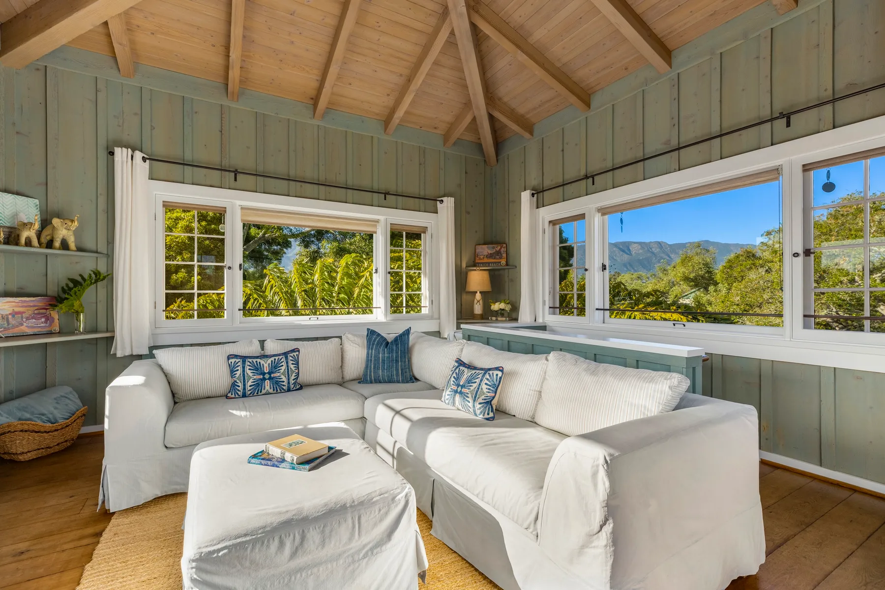 A bright living room with white seating and wide windows overlooking greenery.
