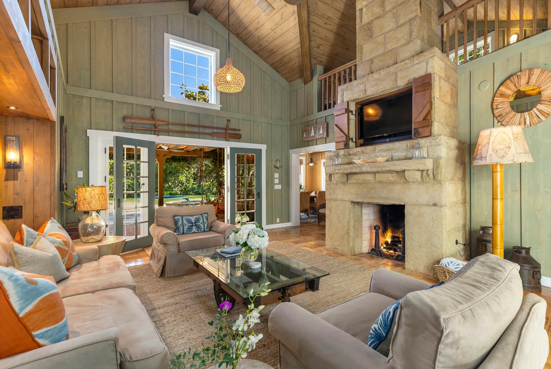 A spacious living room with seating, a stone fireplace, and large glass doors.