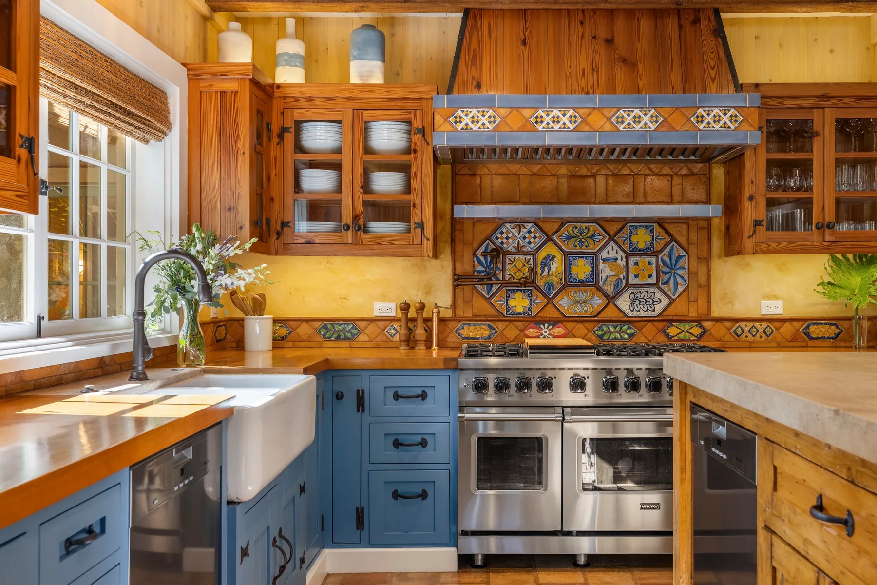 A wood-paneled kitchen with blue cabinets, a farmhouse sink, and a stainless steel range.