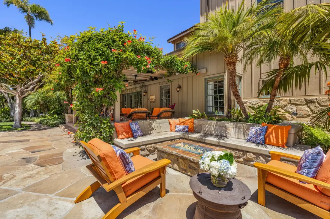 An outdoor patio seating area with a low fire pit and surrounding plants.