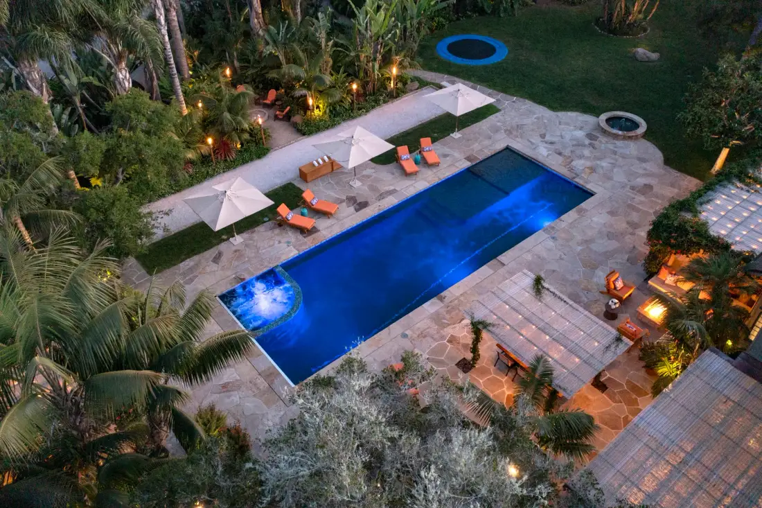 A swimming pool sits in a landscaped garden with lounge seating and umbrellas.