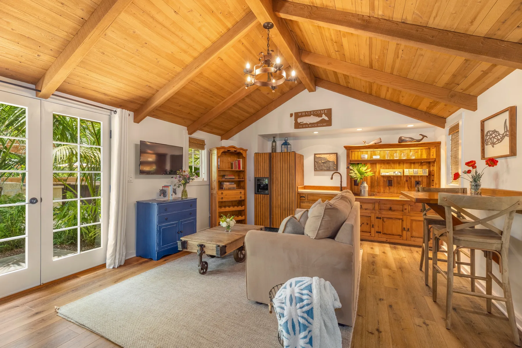 A living room with a vaulted wooden ceiling, seating, and a kitchen counter.