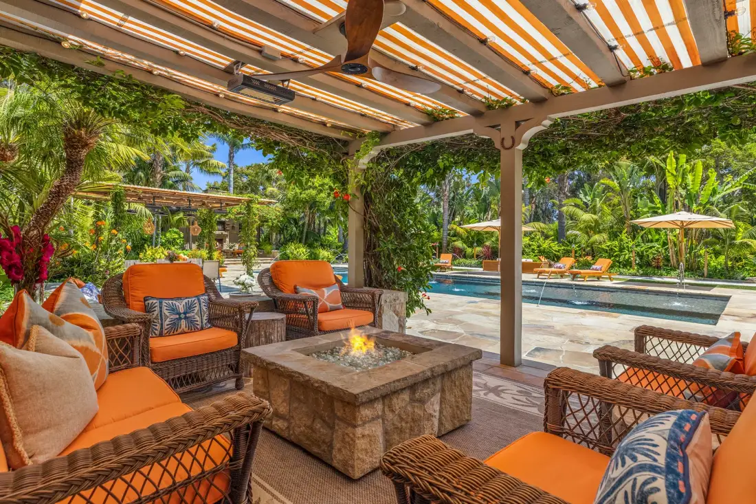 A shaded outdoor seating area overlooks a swimming pool and lush garden.