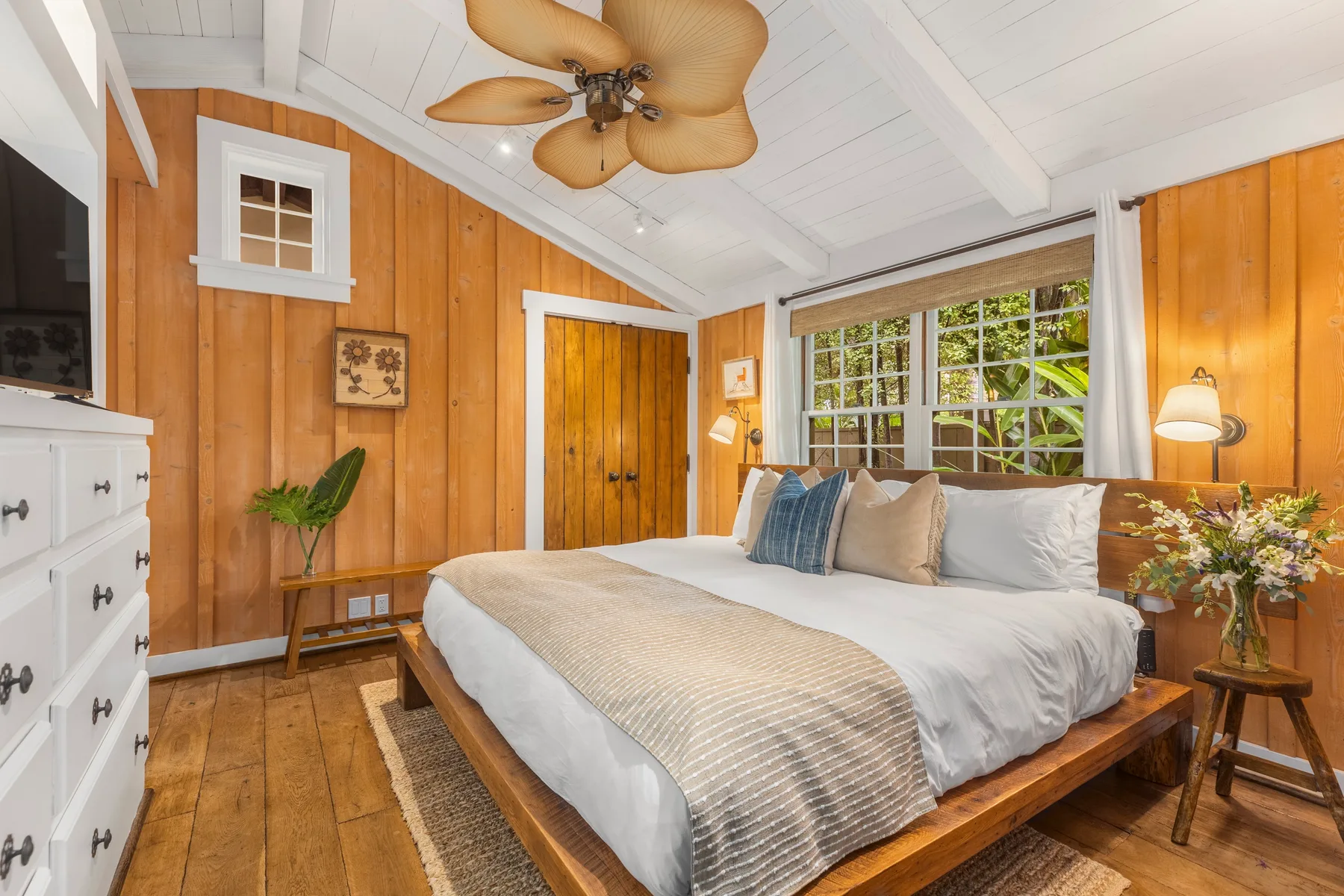 A bedroom with a wooden bed, white bedding, and a large window.