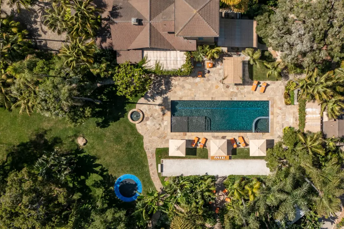 An aerial view shows an outdoor swimming pool surrounded by paving and greenery.