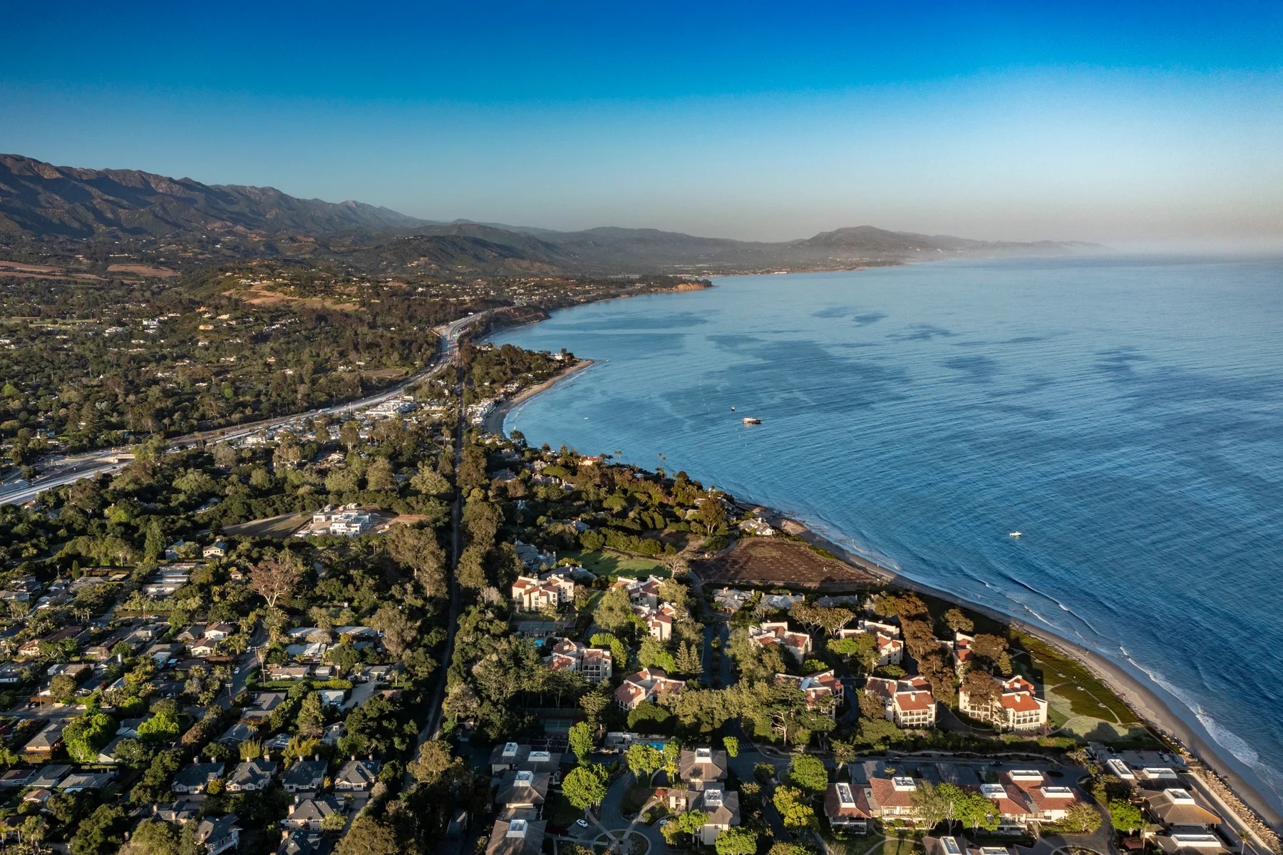 An aerial view of a coastal neighborhood beside a curving shoreline and blue water.