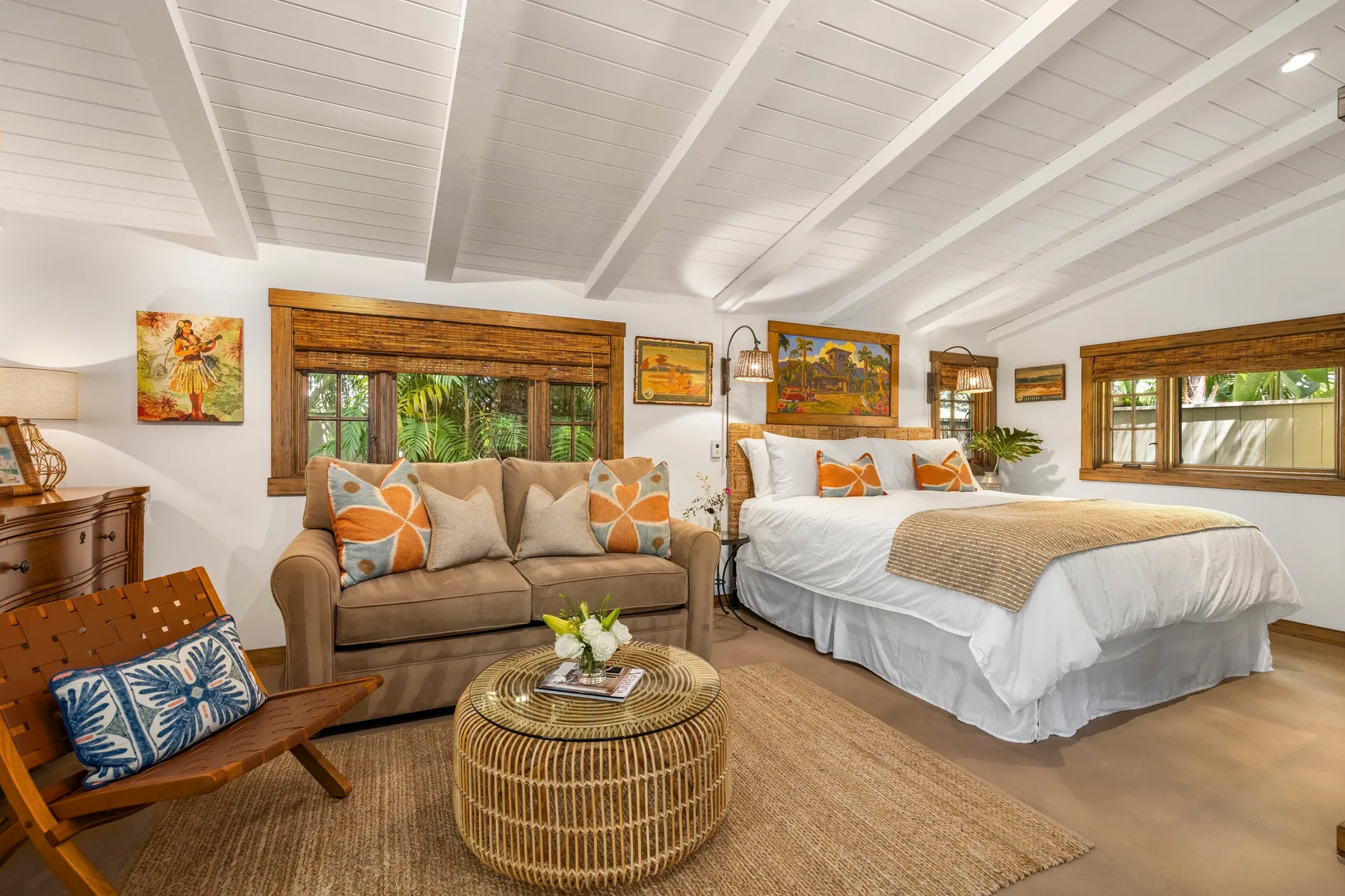 A bedroom with a bed, a sofa, and windows overlooking greenery.