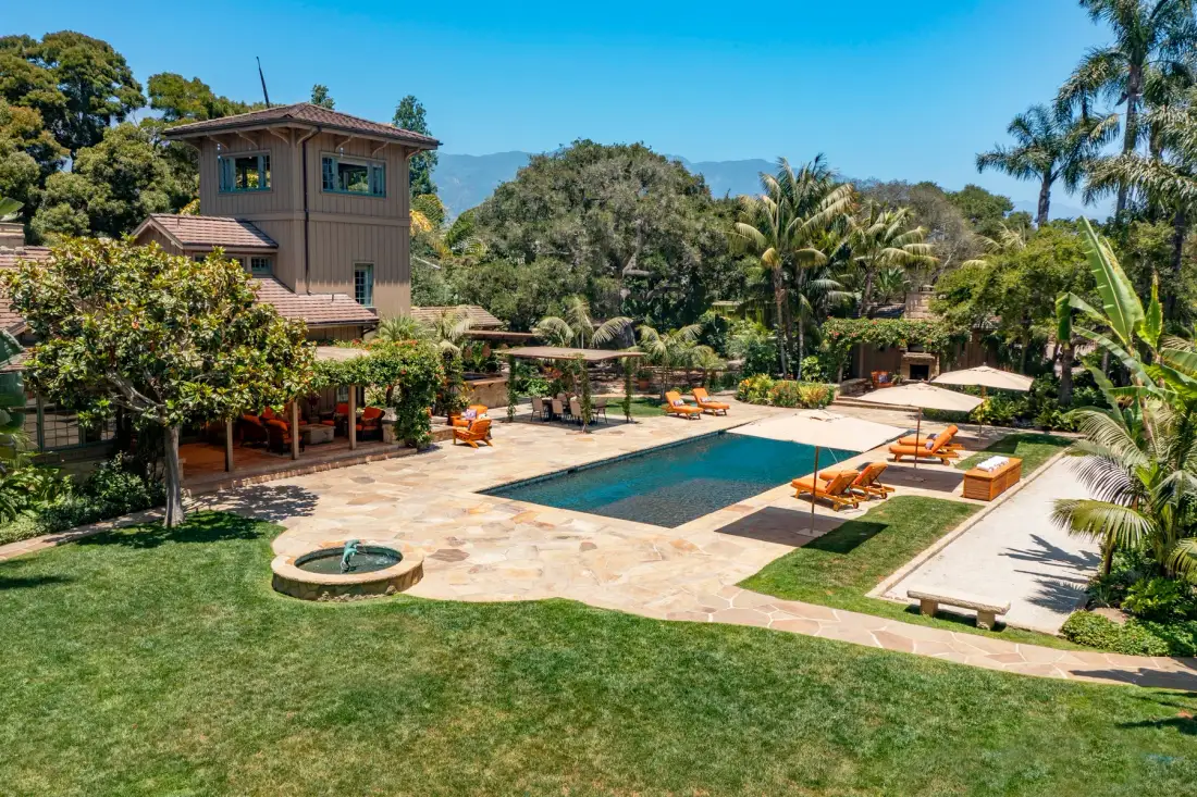 Outdoor pool area with a paved patio, lounge seating, and surrounding gardens.
