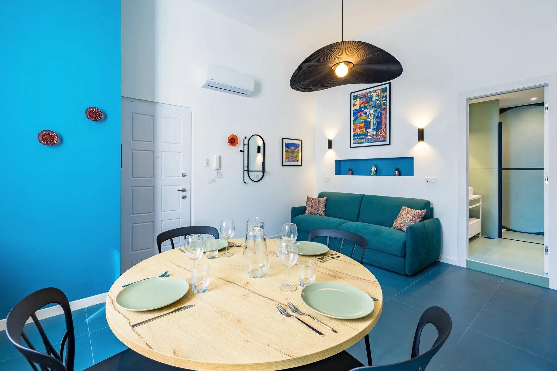 A dining area with a round table set with dishes beside a teal sofa.