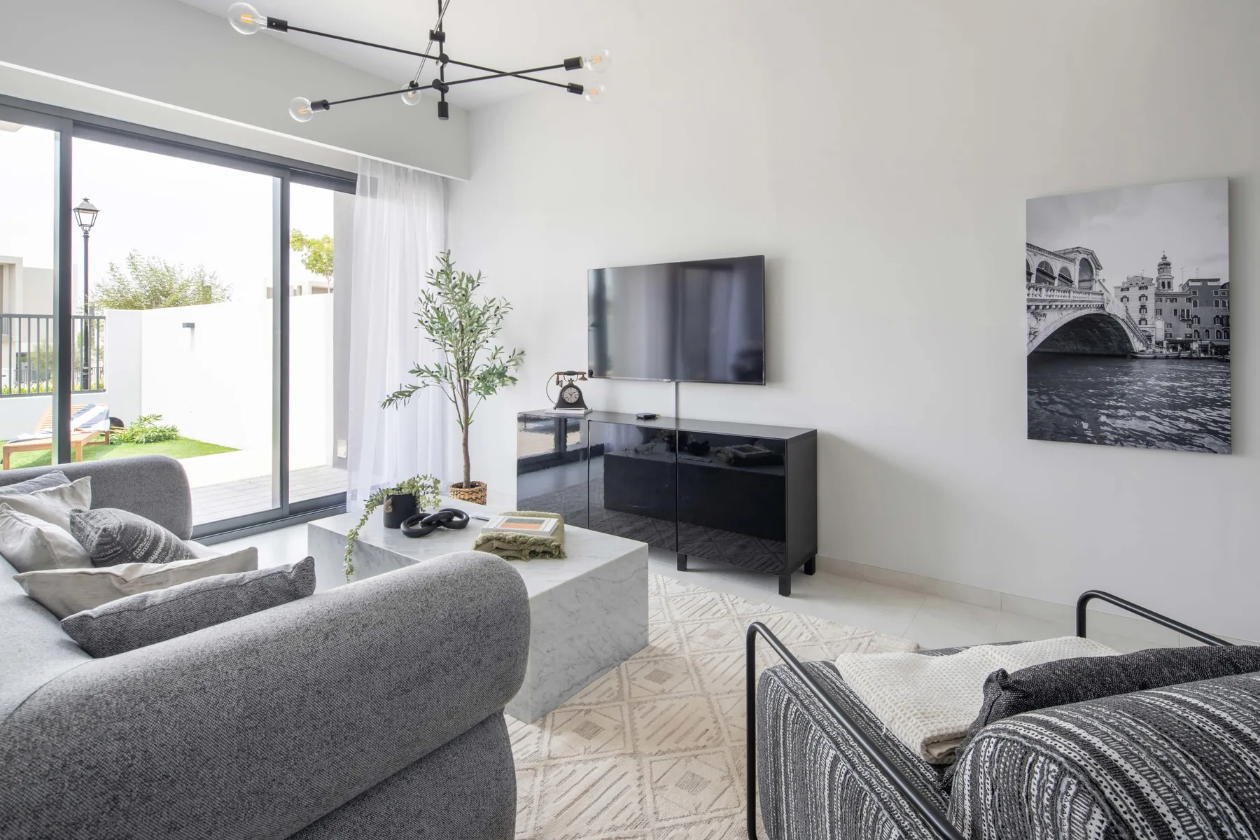 Una sala luminosa con asientos grises, un televisor y puertas corredizas de vidrio.