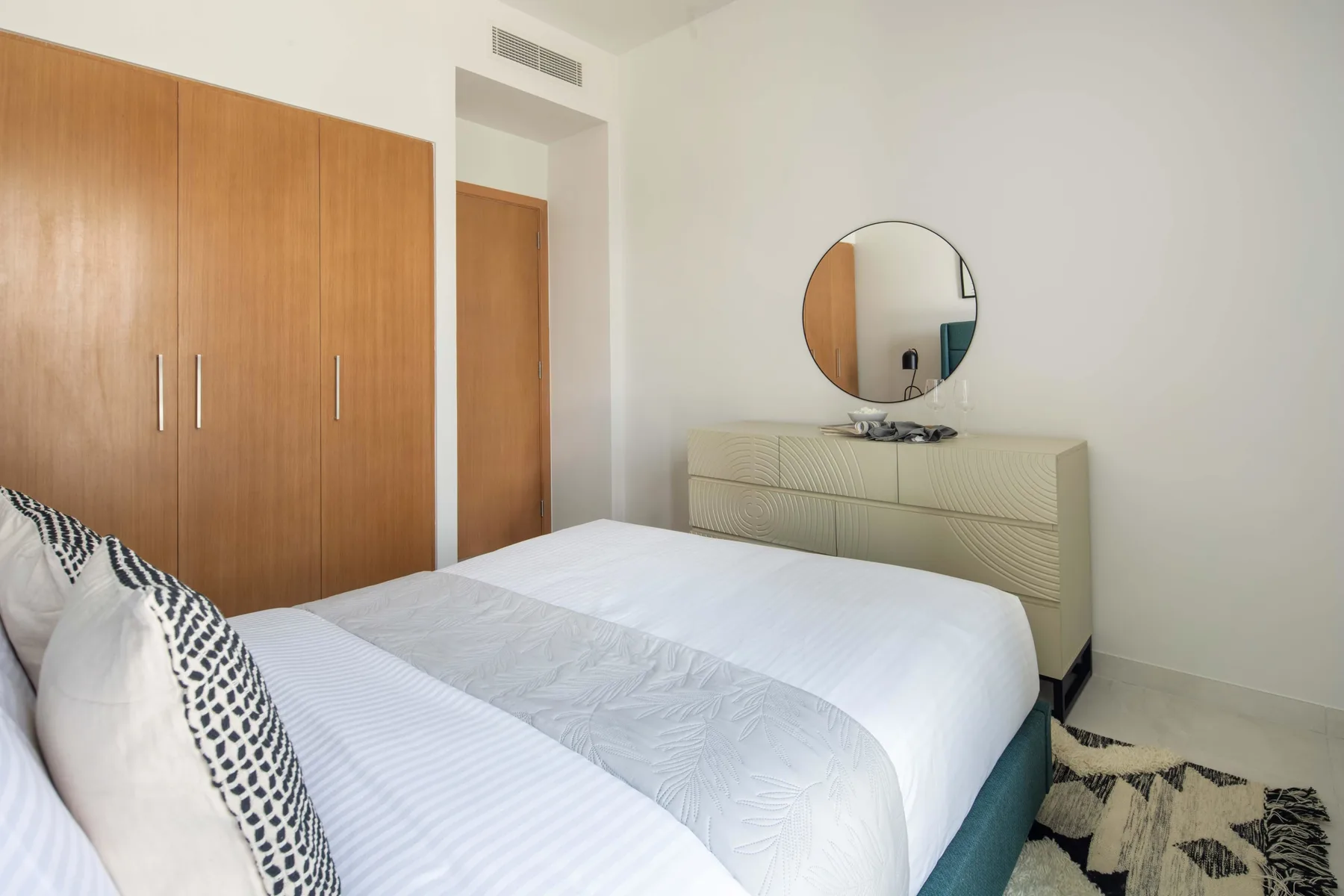 Un dormitorio con una cama, armarios de madera y una cómoda con un espejo redondo.