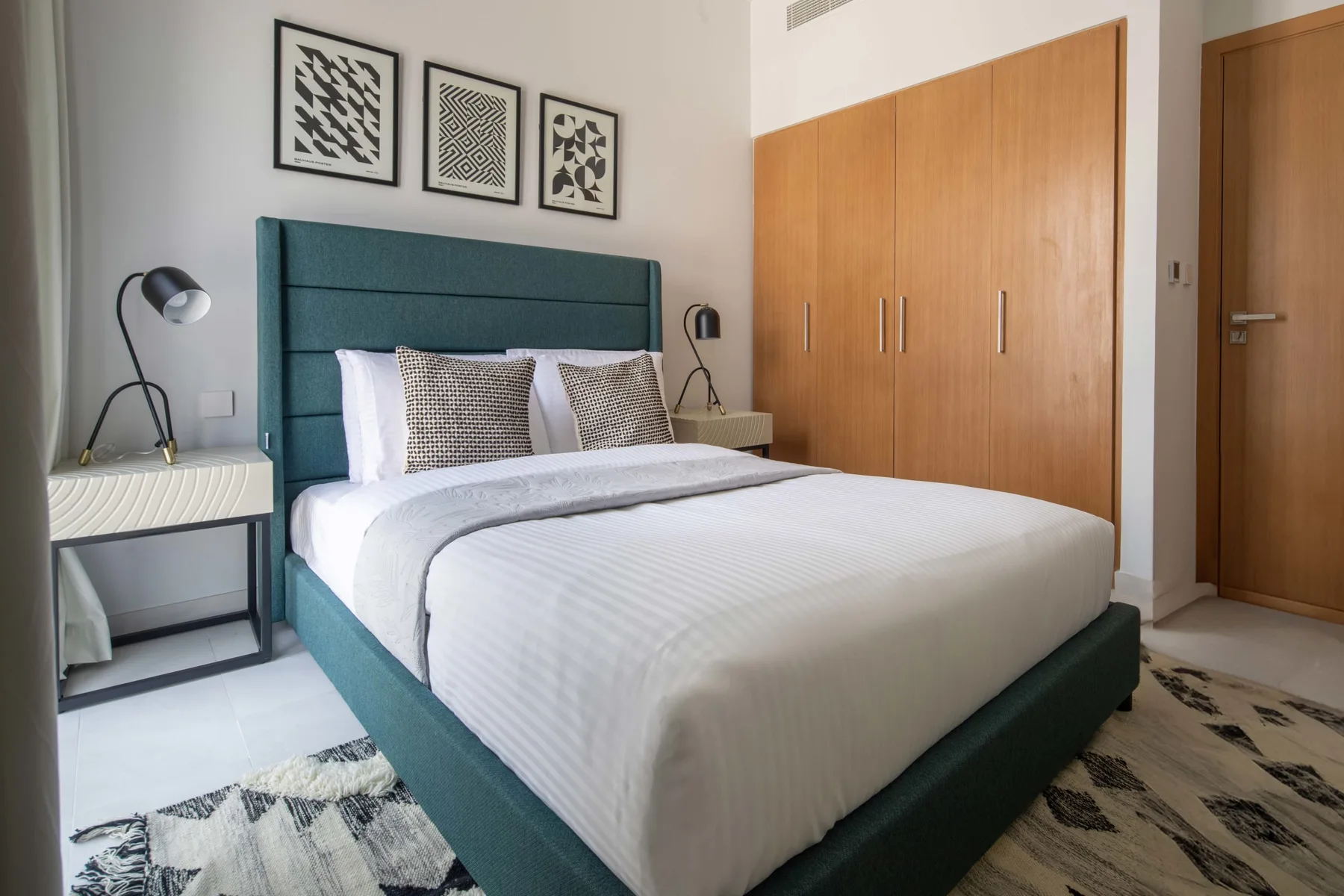 Un dormitorio con una cama bien hecha, mesitas de noche y cuadros enmarcados.