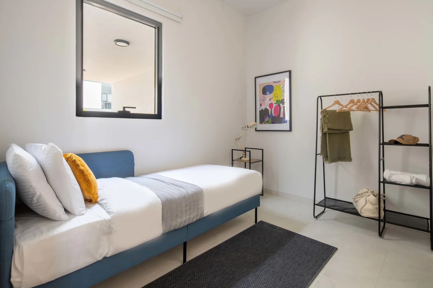 Un dormitorio con una cama, un perchero y estantes abiertos.