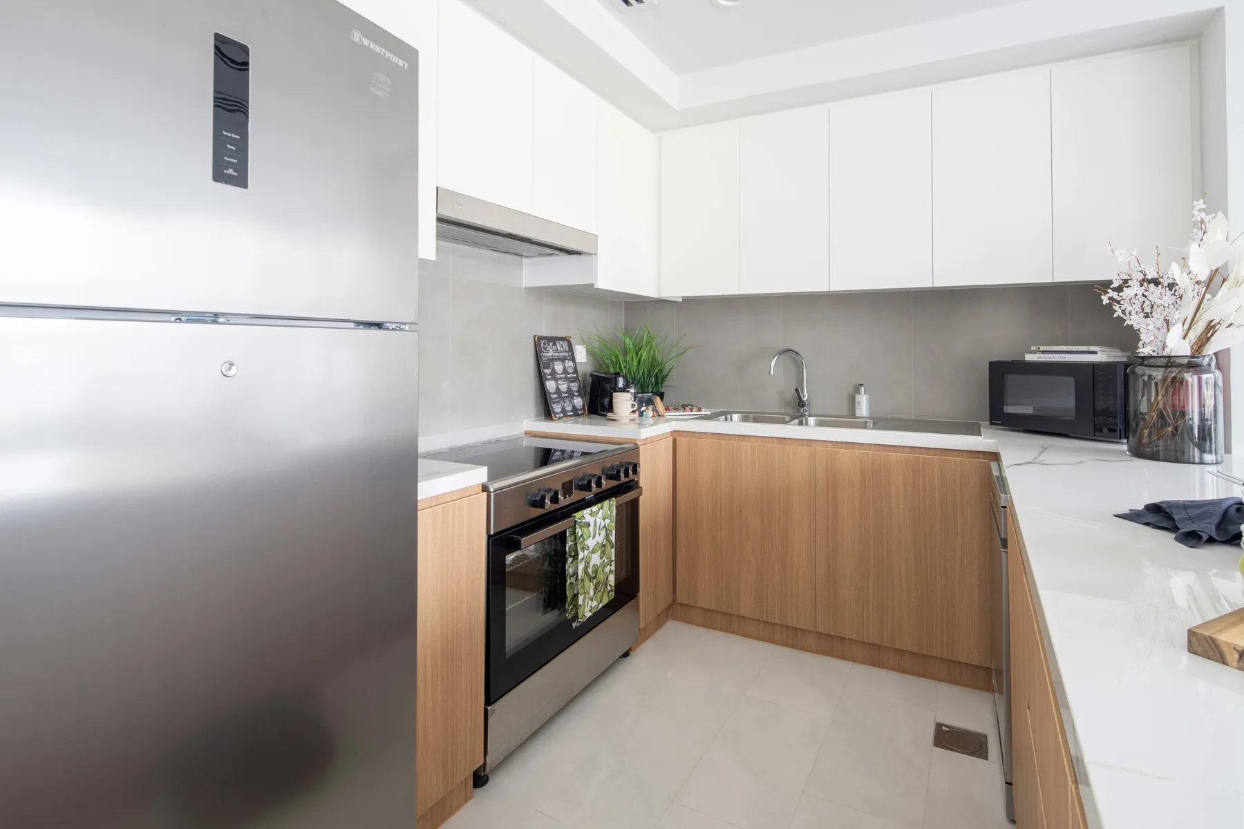 Una cocina moderna con gabinetes blancos, gabinetes inferiores en tono madera y un refrigerador de acero inoxidable.