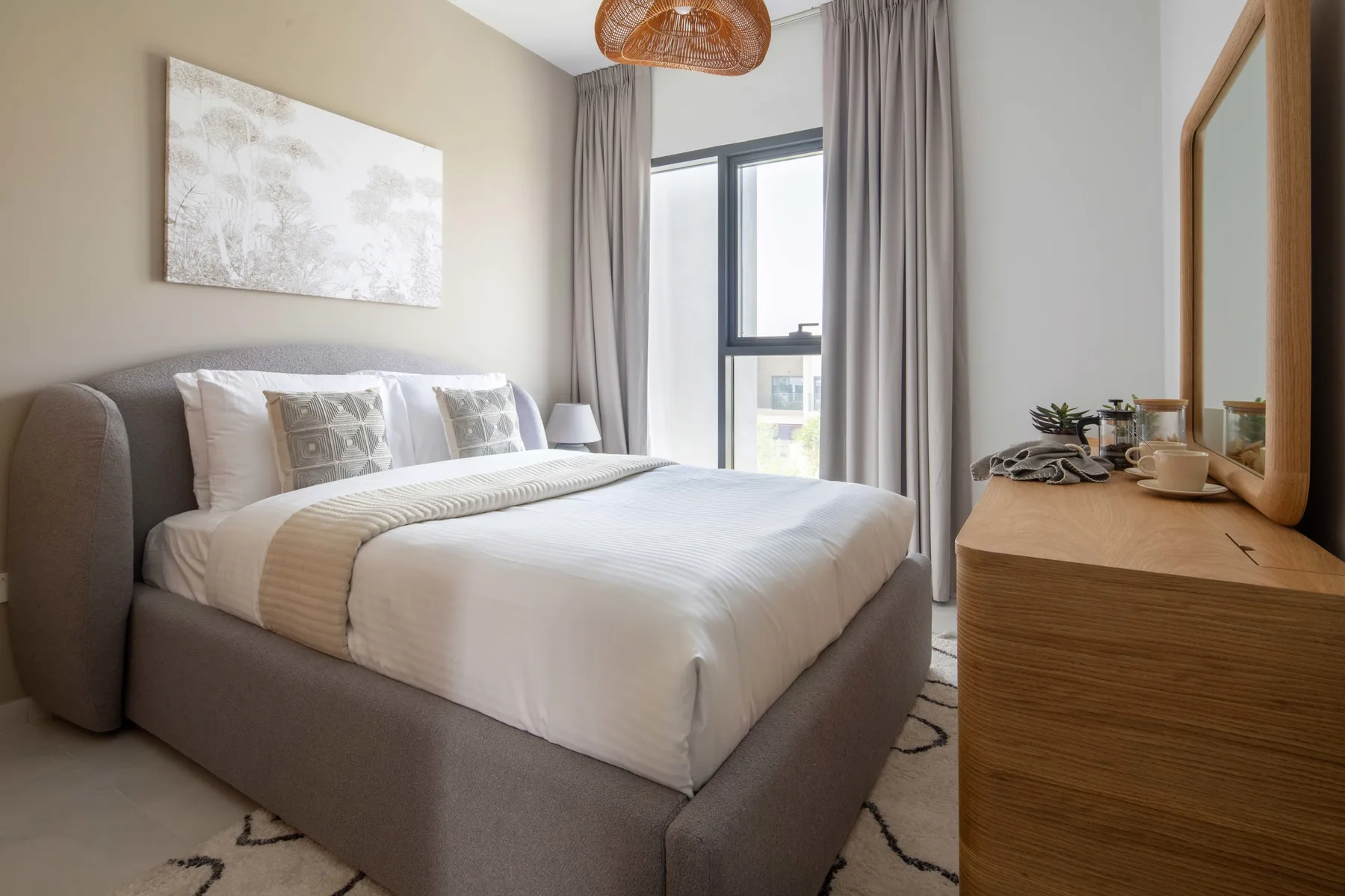 Un dormitorio con una cama bien hecha junto a una ventana con cortinas claras.