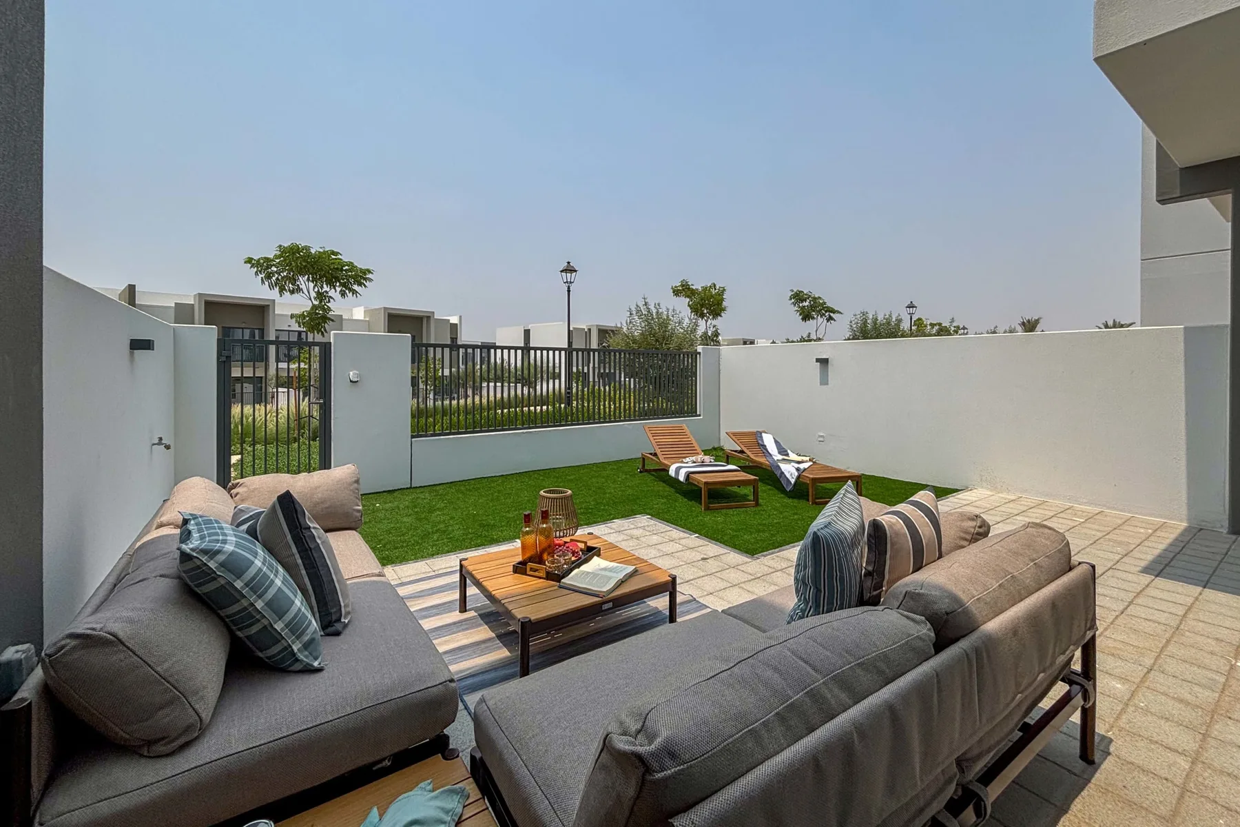 Un patio exterior con asientos acolchados, una mesa de centro y tumbonas junto al césped.