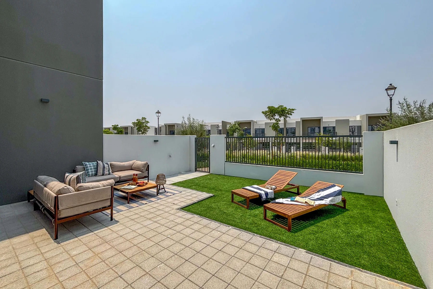 Un patio exterior con asientos, mesas bajas y una pequeña zona de césped.