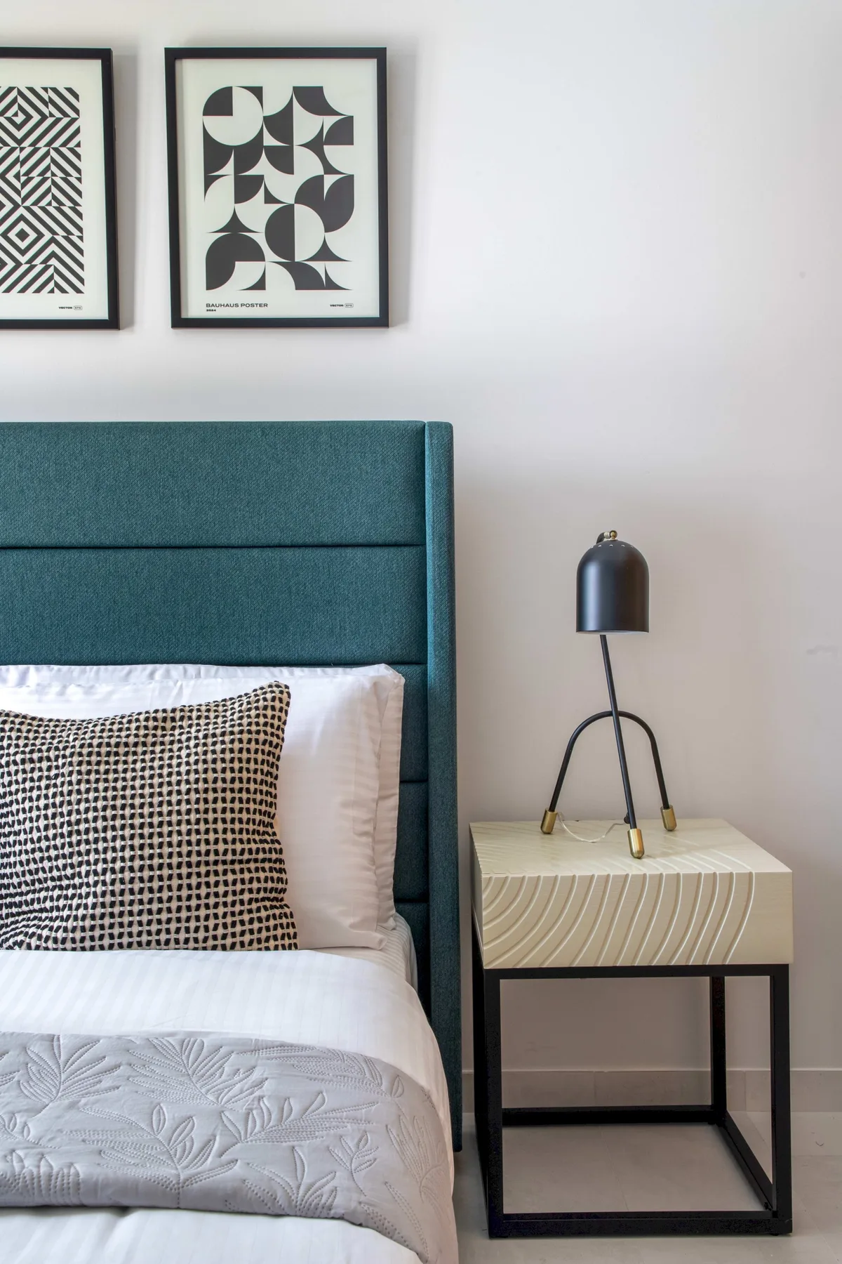 Dormitorio con cabecero tapizado en verde azulado, ropa de cama estampada y mesa auxiliar.