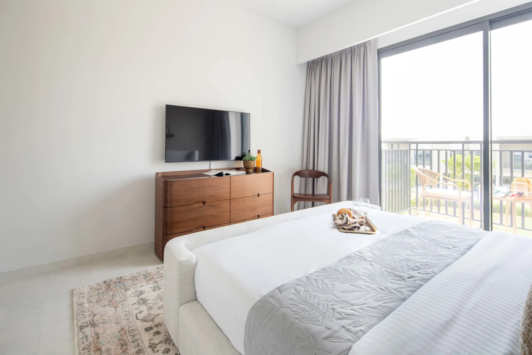 Un dormitorio luminoso con cama, televisor y puertas corredizas de vidrio que dan a un balcón.