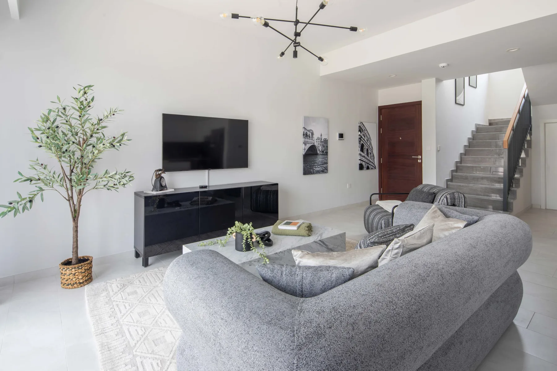 Una sala de estar con asientos grises, un televisor y una escalera.