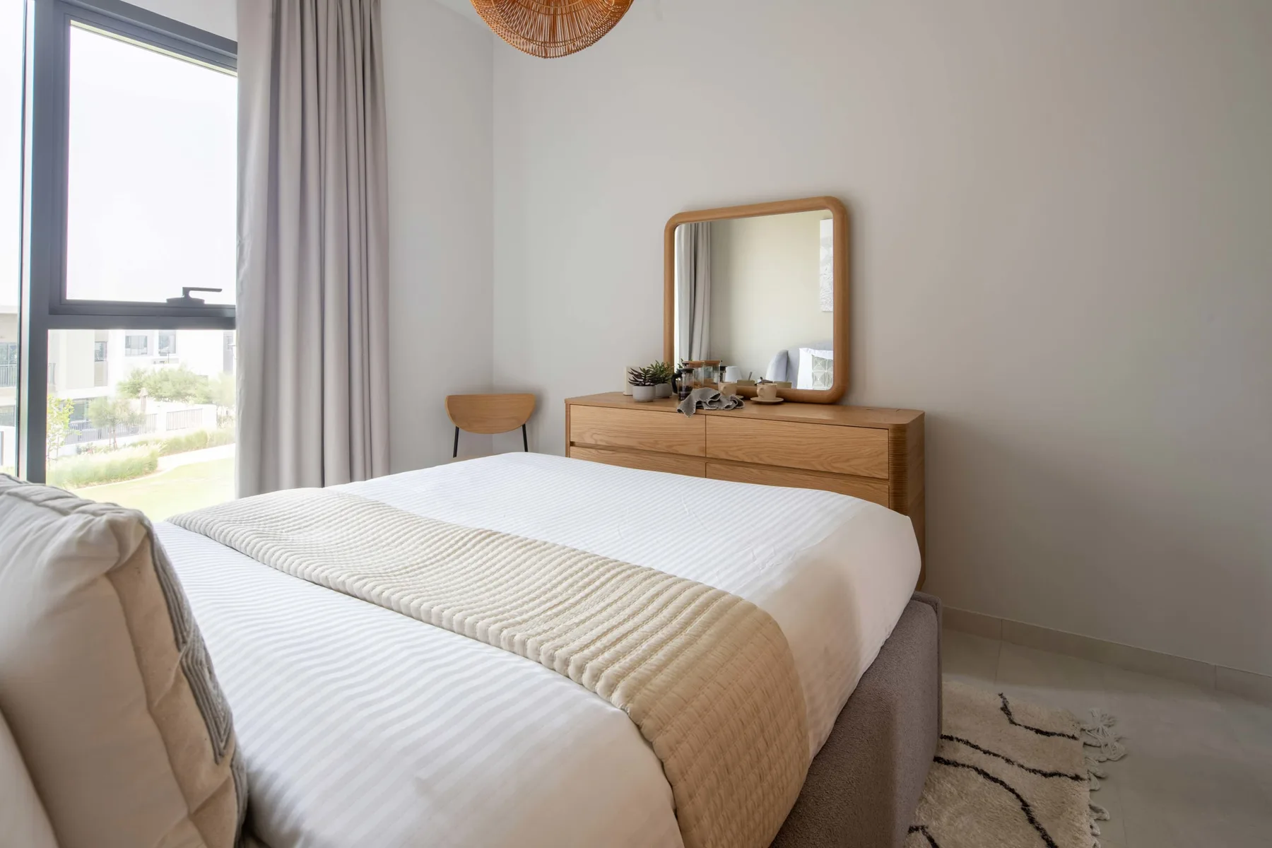 Un dormitorio luminoso con una cama tendida, una cómoda y una ventana grande.