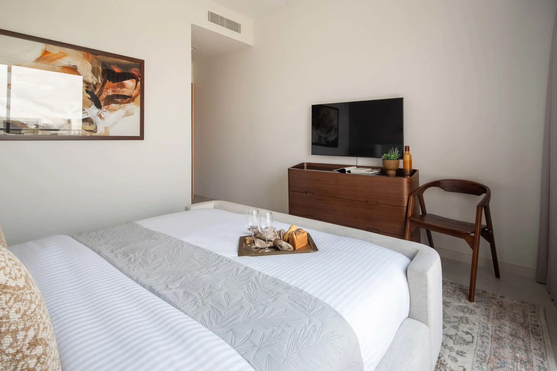 Un dormitorio con una cama bien tendida, una cómoda y un televisor.