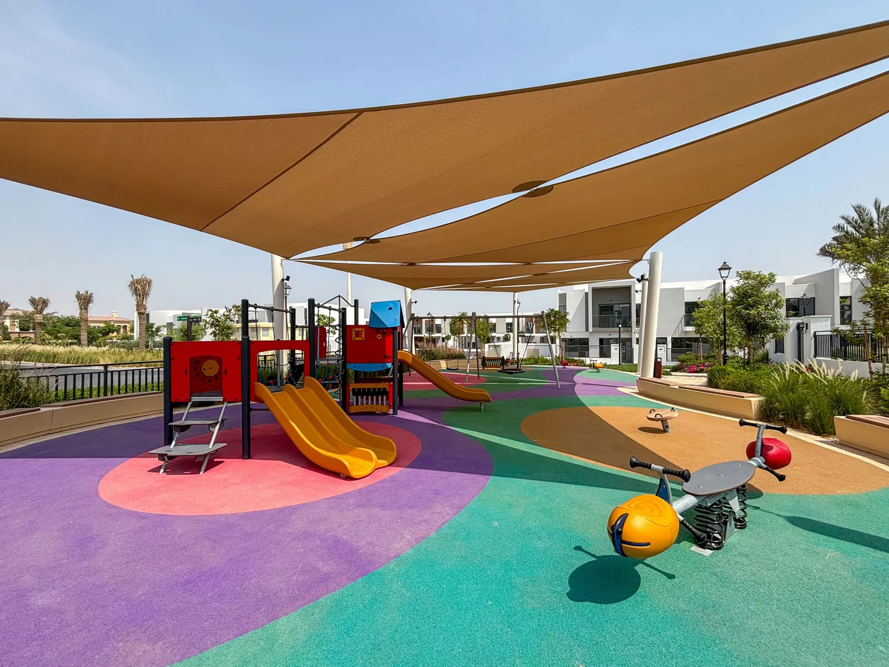 Un parque infantil al aire libre tiene juegos coloridos bajo grandes toldos.