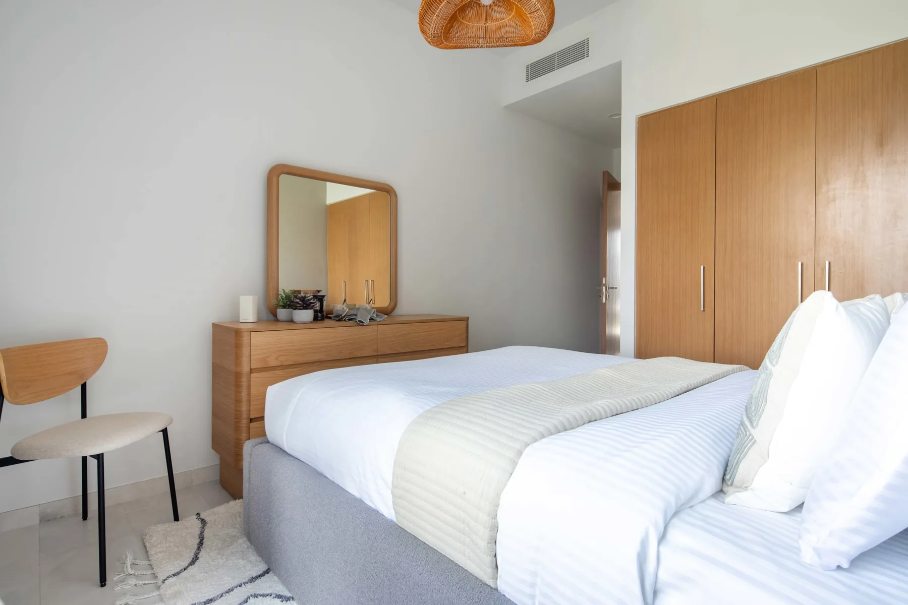 Un dormitorio luminoso con una cama, un armario de madera y una cómoda.