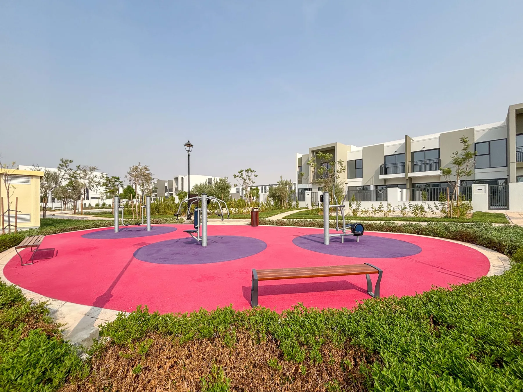 Un parque infantil al aire libre tiene suelo de colores, juegos para trepar y bancos cercanos.